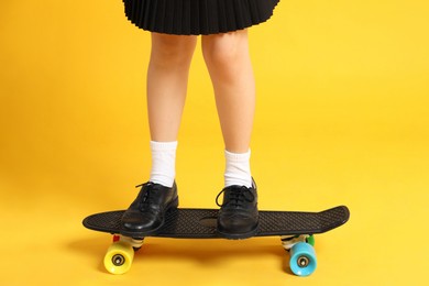 Little girl standing on penny board against yellow background, closeup