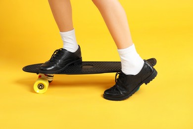 Little girl with penny board on yellow background, closeup