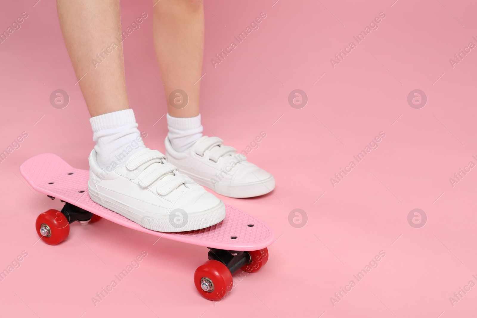 Photo of Little girl with penny board on pink background, closeup. Space for text