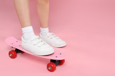 Photo of Little girl with penny board on pink background, closeup. Space for text