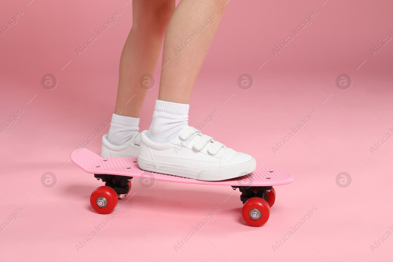 Photo of Little girl with penny board on pink background, closeup