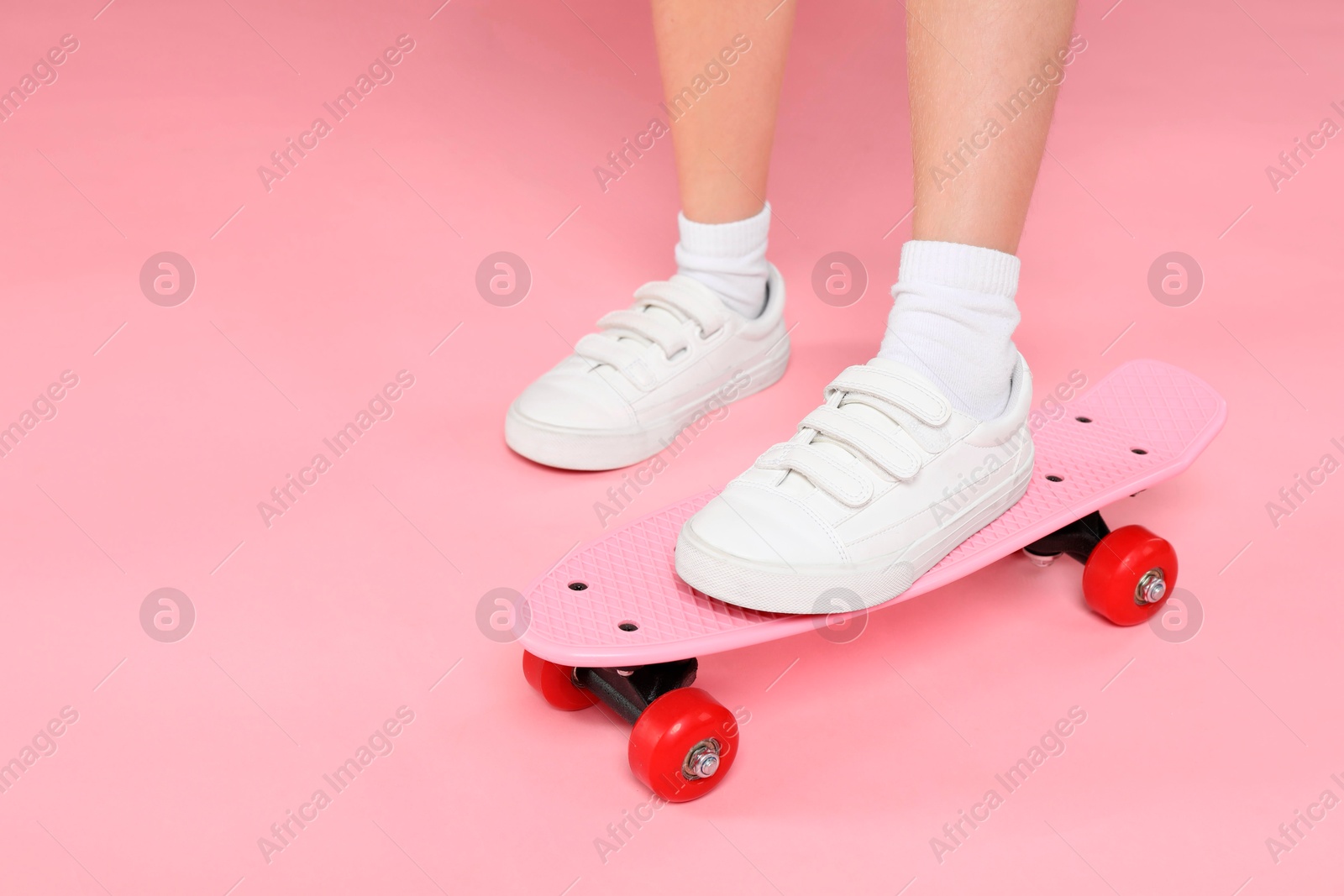 Photo of Little girl with penny board on pink background, closeup. Space for text