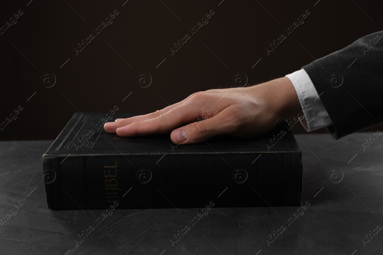 Photo of Man taking oath with his hand on Bible at black table, closeup