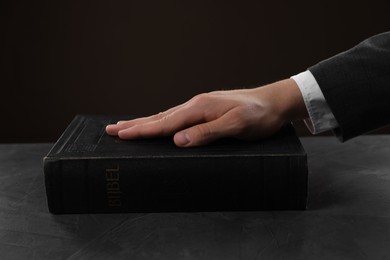 Photo of Man taking oath with his hand on Bible at black table, closeup