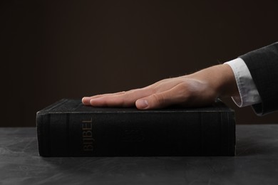 Photo of Man taking oath with his hand on Bible at black table, closeup