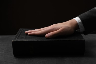 Photo of Man taking oath with his hand on Bible at black table, closeup