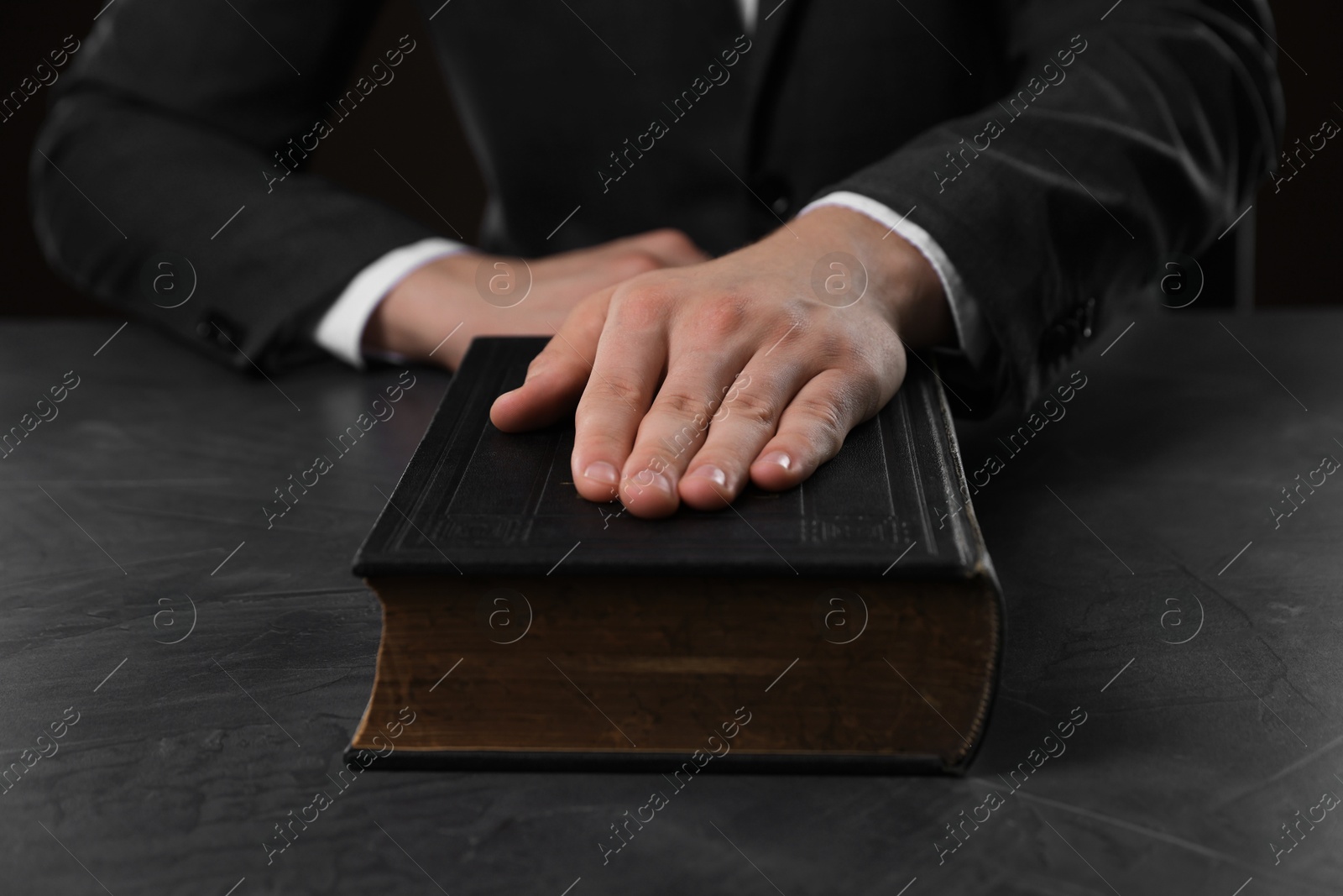 Photo of Man taking oath with his hand on Bible at black table, closeup