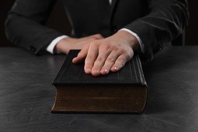 Photo of Man taking oath with his hand on Bible at black table, closeup