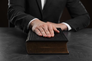 Photo of Man taking oath with his hand on Bible at black table, closeup