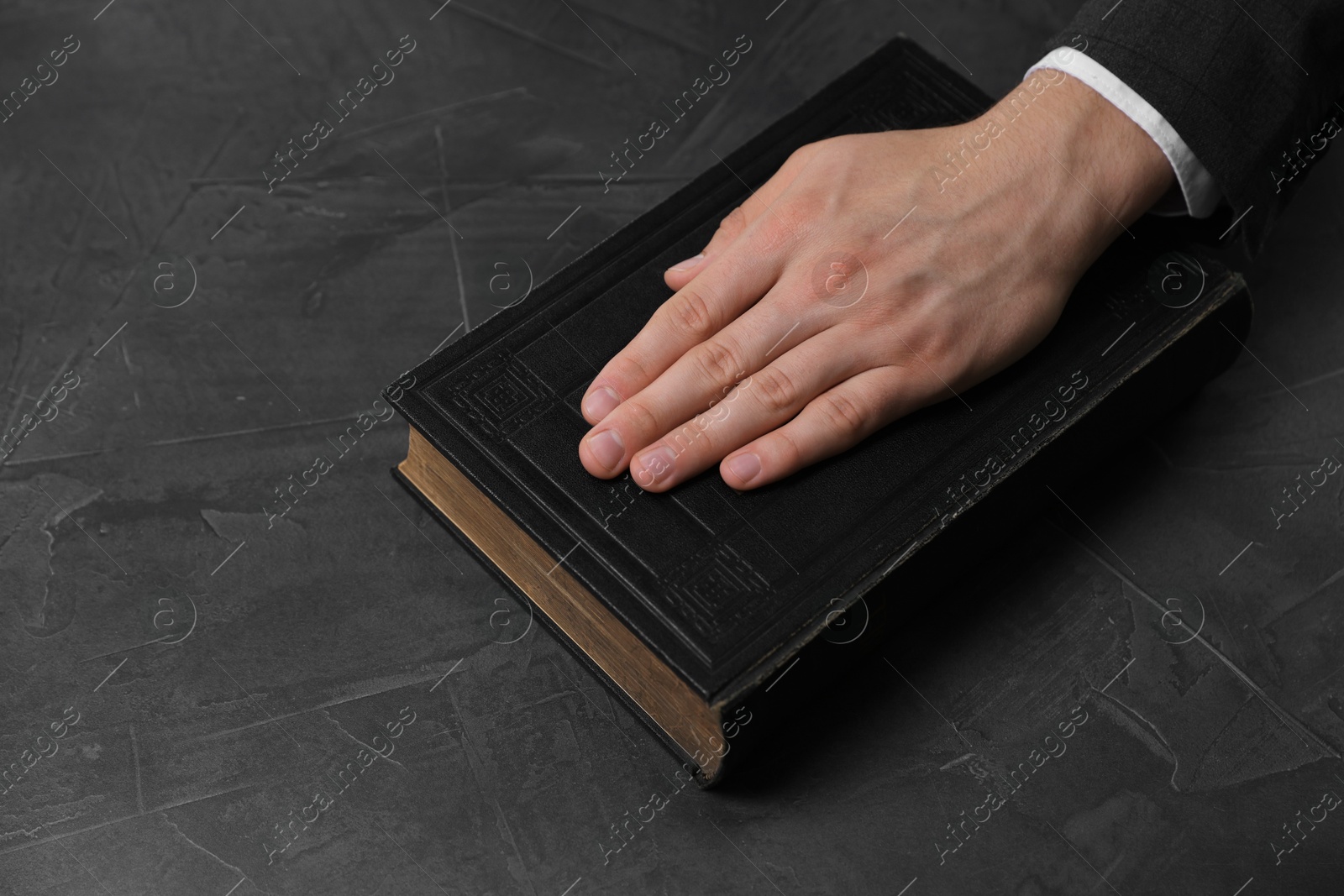 Photo of Man taking oath with his hand on Bible at black table, closeup