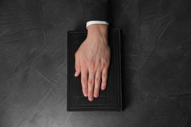 Photo of Man taking oath with his hand on Bible at black table, top view