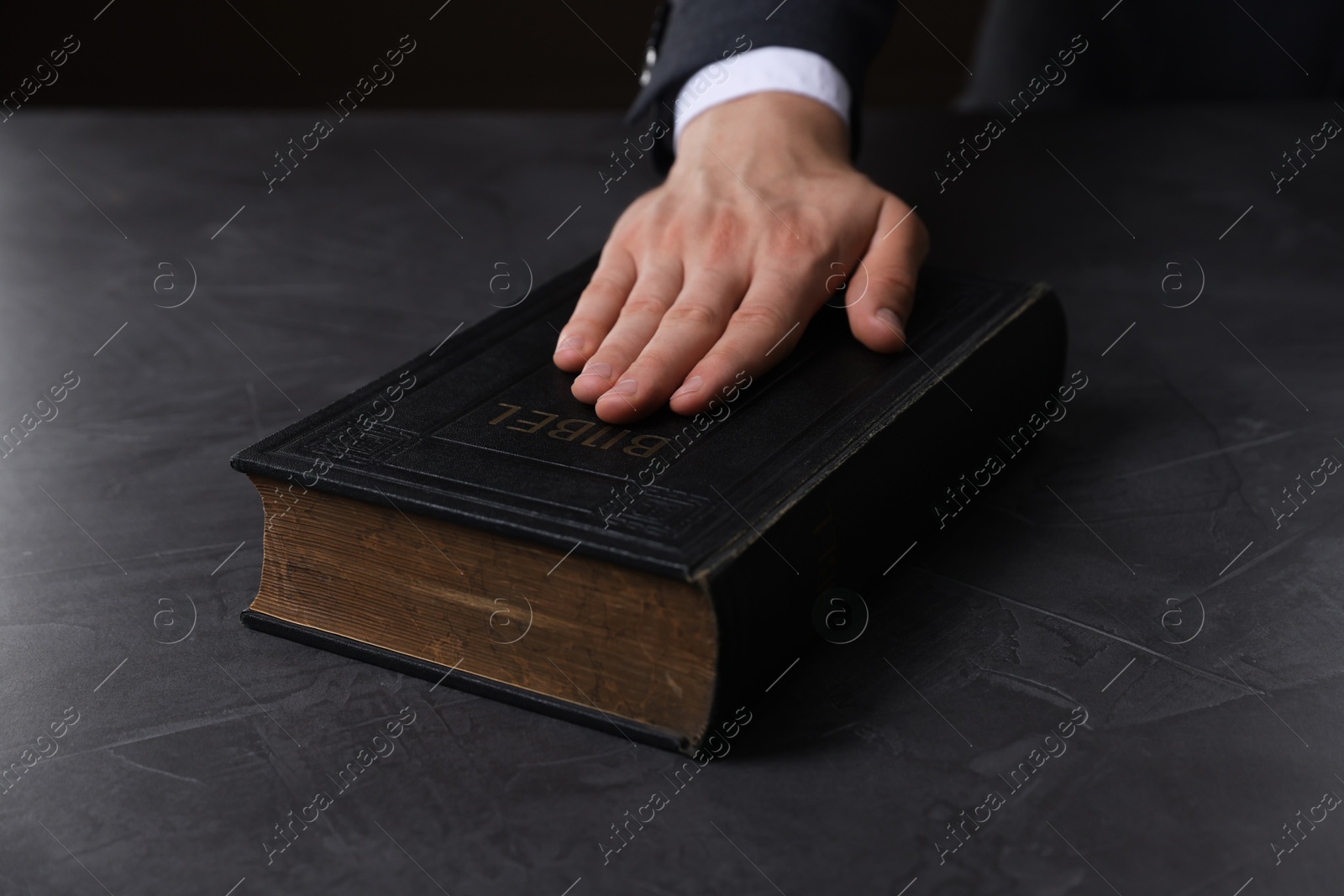 Photo of Man taking oath with his hand on Bible at black table, closeup