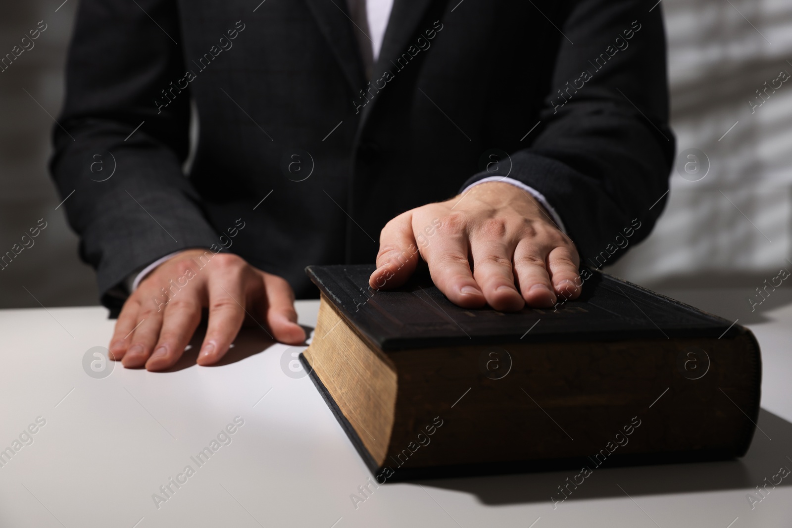 Photo of Man taking oath with his hand on Bible at white table, closeup