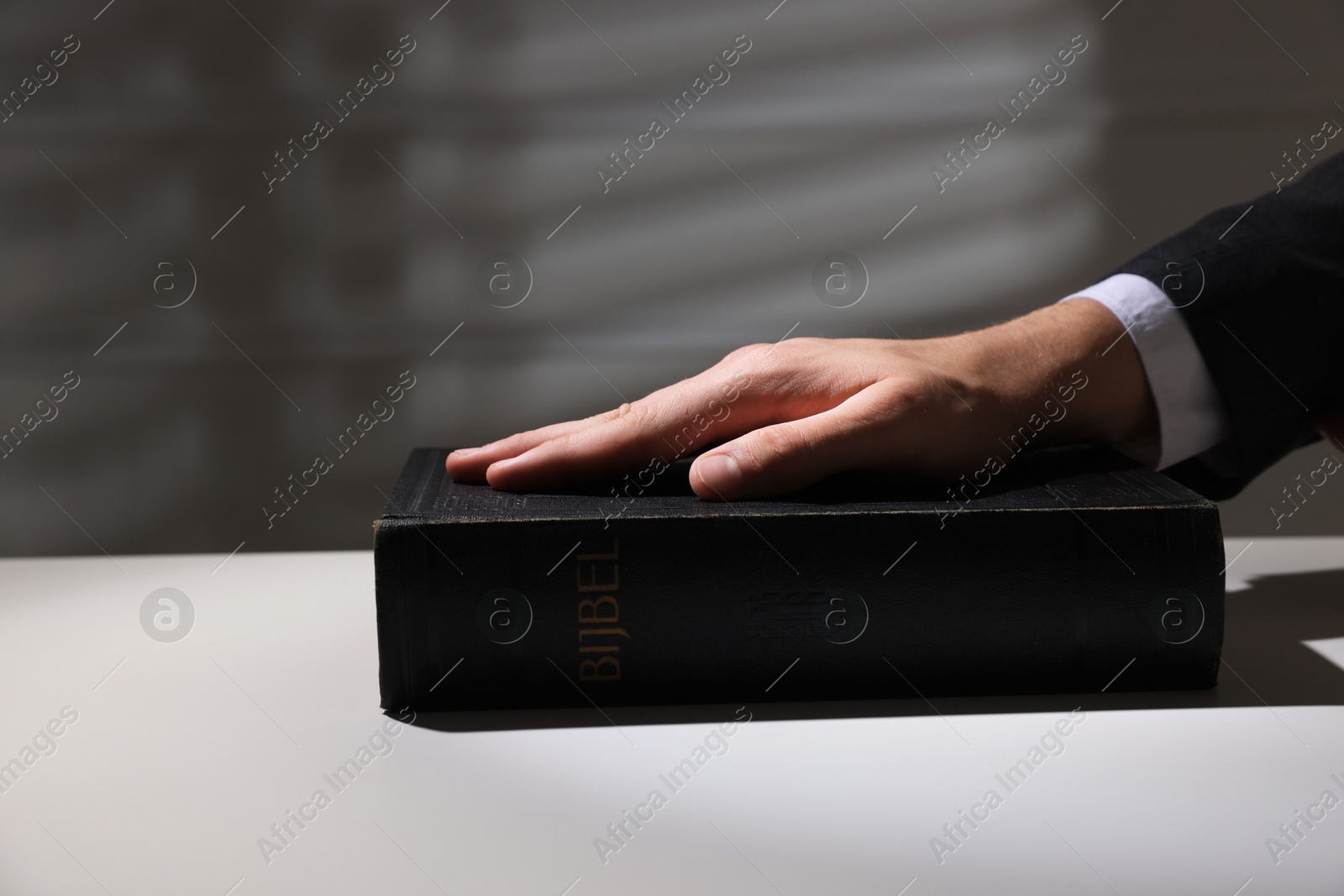 Photo of Man taking oath with his hand on Bible at white table, closeup