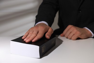 Photo of Man taking oath with his hand on Bible at white table, closeup