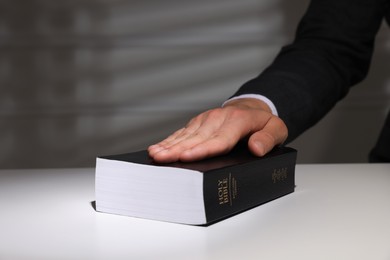 Photo of Man taking oath with his hand on Bible at white table, closeup