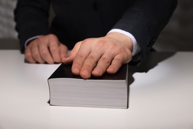 Photo of Man taking oath with his hand on Bible at white table, closeup