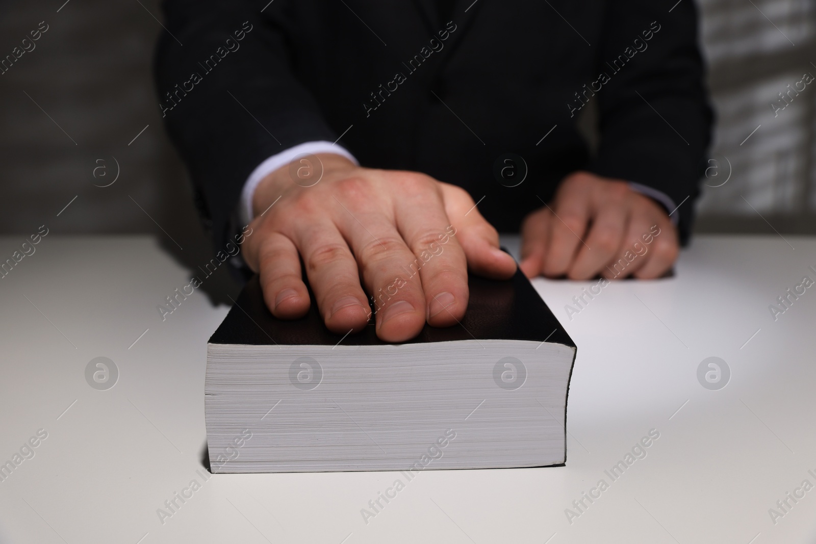 Photo of Man taking oath with his hand on Bible at white table, closeup