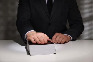 Photo of Man taking oath with his hand on Bible at white table, closeup