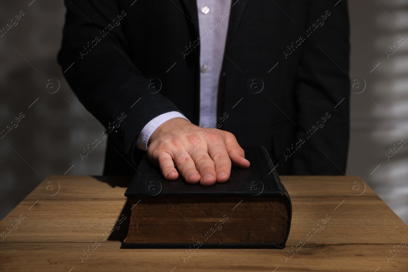 Photo of Man taking oath with his hand on Bible at wooden table, closeup