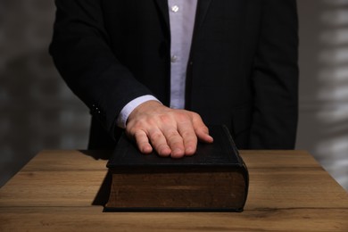 Photo of Man taking oath with his hand on Bible at wooden table, closeup