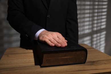 Photo of Man taking oath with his hand on Bible at wooden table, closeup