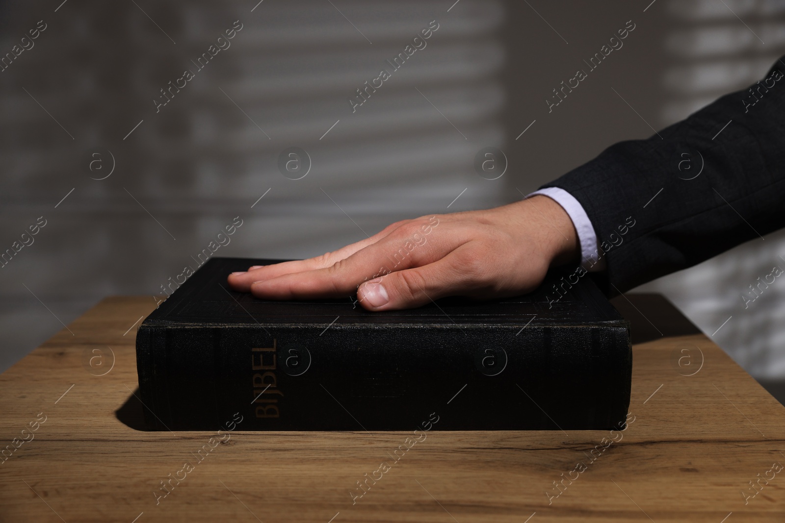 Photo of Man taking oath with his hand on Bible at wooden table, closeup