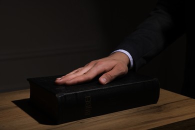 Photo of Man taking oath with his hand on Bible at wooden table, closeup