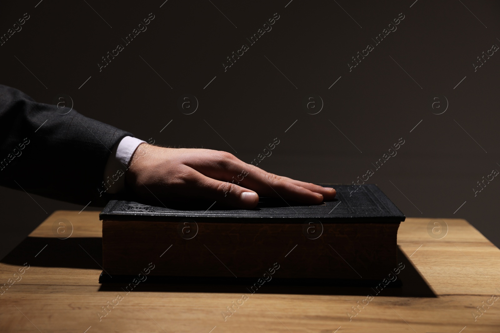 Photo of Man taking oath with his hand on Bible at wooden table, closeup