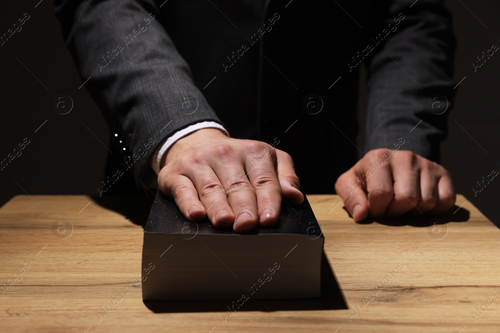 Photo of Man taking oath with his hand on Bible at wooden table, closeup