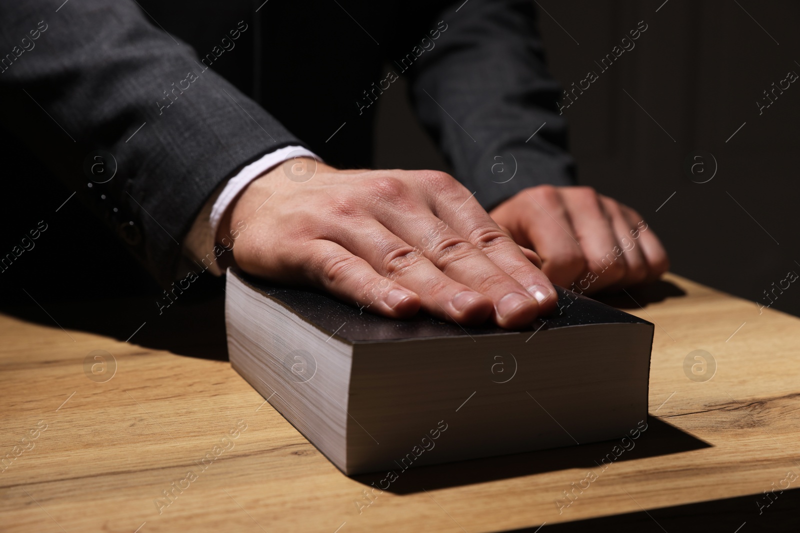 Photo of Man taking oath with his hand on Bible at wooden table, closeup