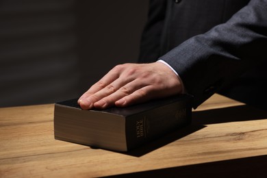 Photo of Man taking oath with his hand on Bible at wooden table, closeup