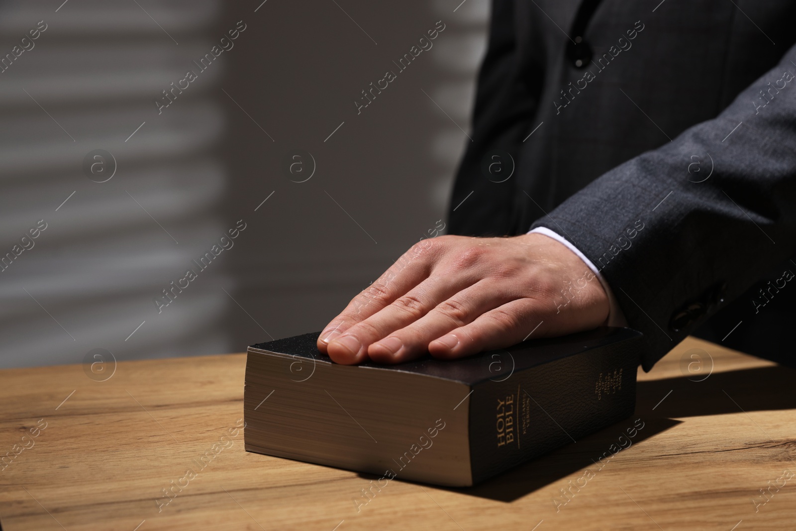 Photo of Man taking oath with his hand on Bible at wooden table, closeup