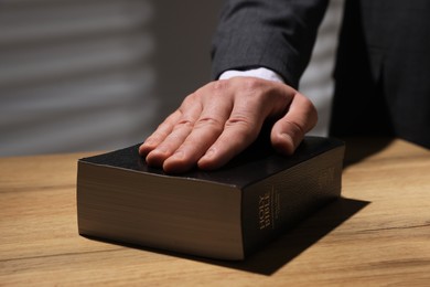 Photo of Man taking oath with his hand on Bible at wooden table, closeup