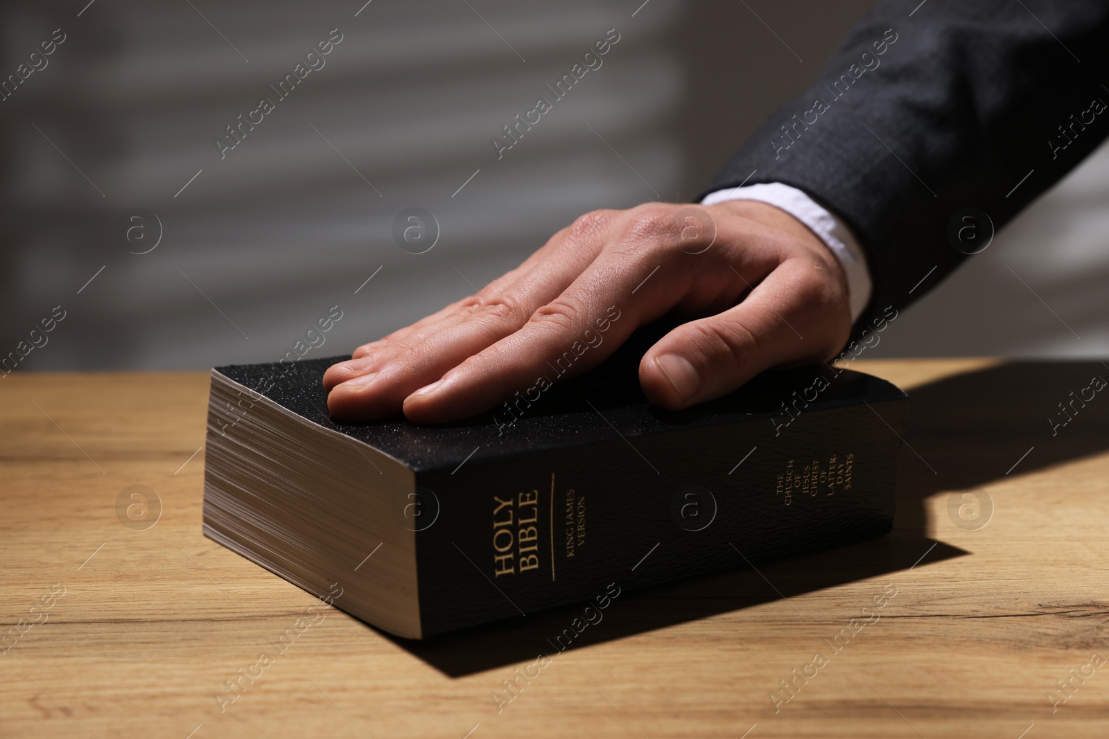 Photo of Man taking oath with his hand on Bible at wooden table, closeup