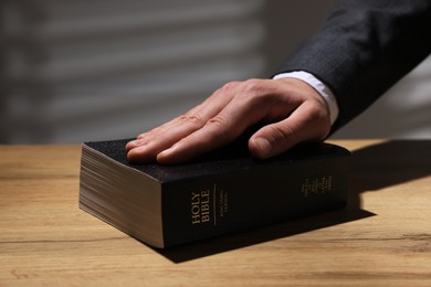 Photo of Man taking oath with his hand on Bible at wooden table, closeup