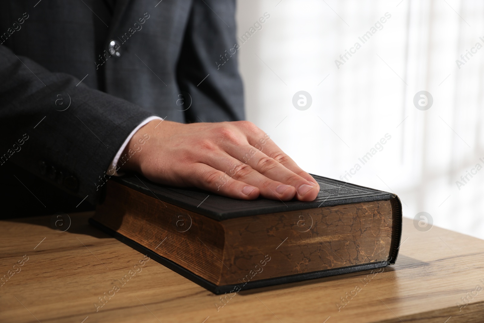 Photo of Man taking oath with his hand on Bible at wooden table, closeup