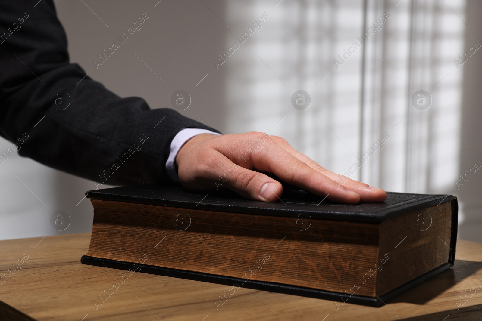 Photo of Man taking oath with his hand on Bible at wooden table, closeup