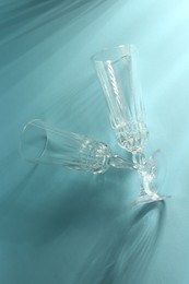 Photo of Two empty wine glasses casting beautiful shadows on light blue background, top view