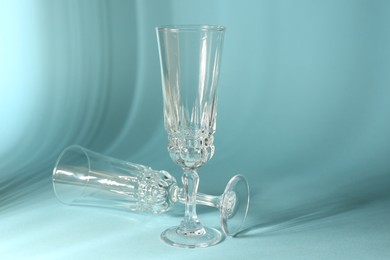 Photo of Two empty wine glasses casting beautiful shadows on light blue background, space for text