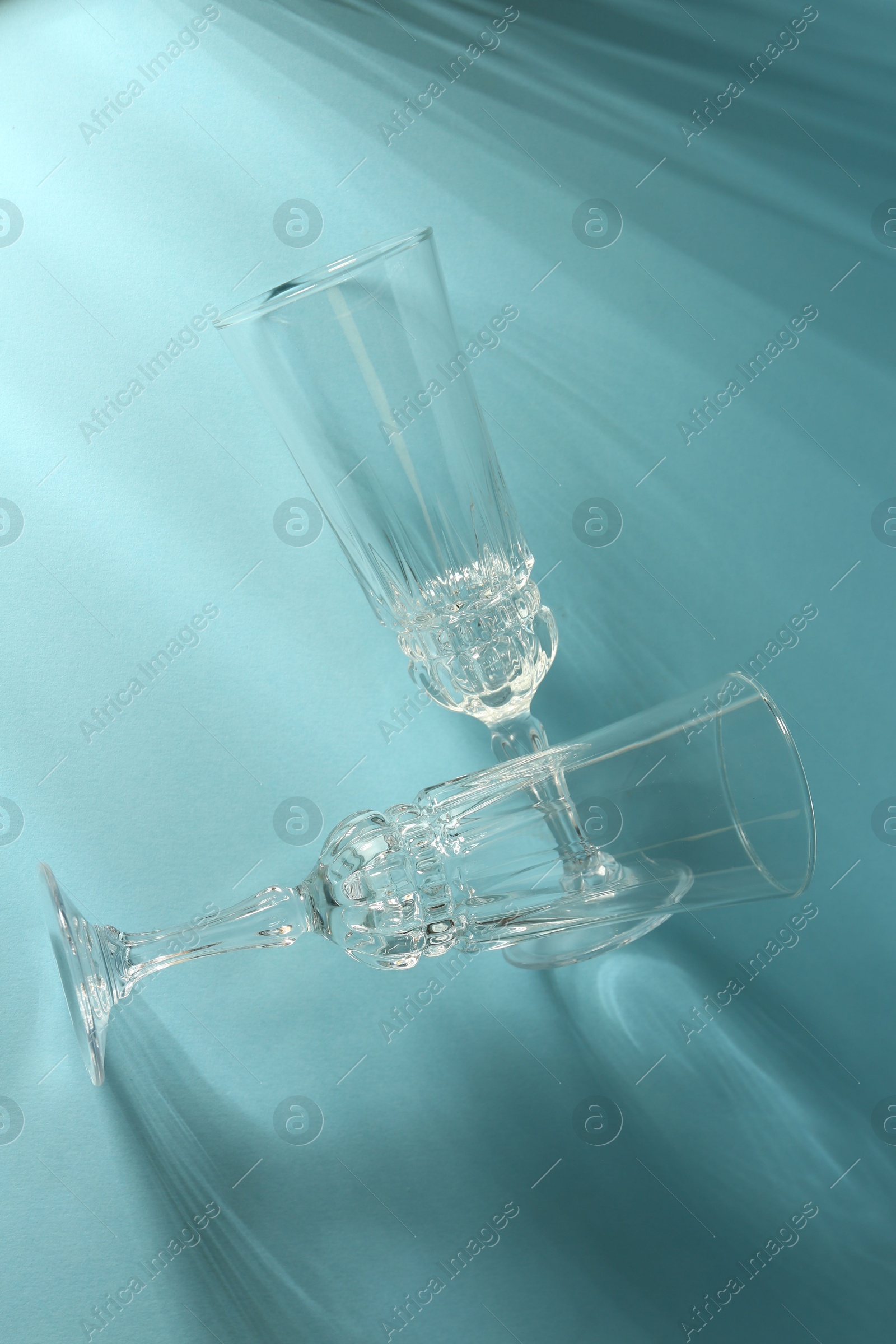 Photo of Two empty wine glasses casting beautiful shadows on light blue background, top view