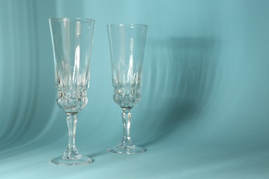 Photo of Two empty wine glasses casting beautiful shadows on light blue background, space for text