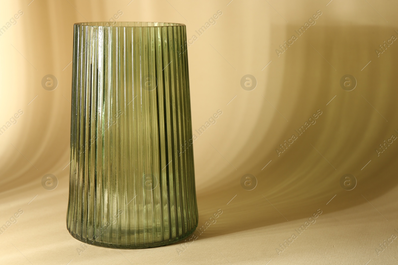 Photo of Empty glass vase casting beautiful shadows on beige background, space for text