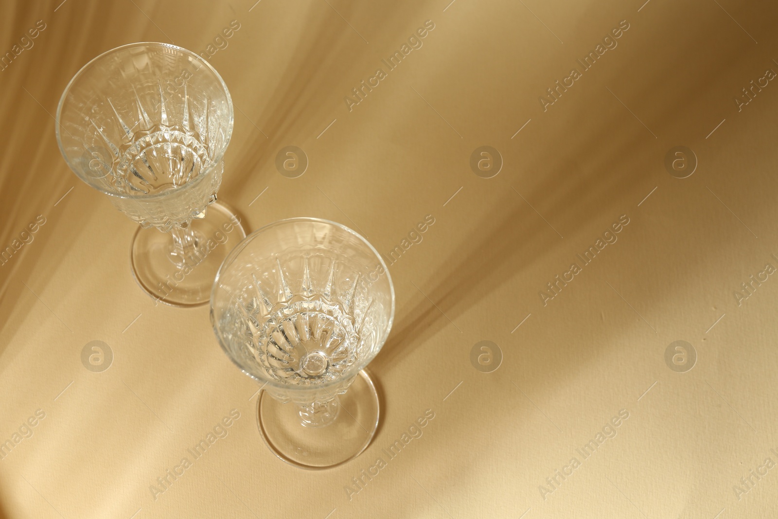 Photo of Two empty wine glasses on beige background, above view. Space for text