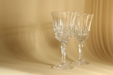 Photo of Two empty wine glasses on beige background, space for text