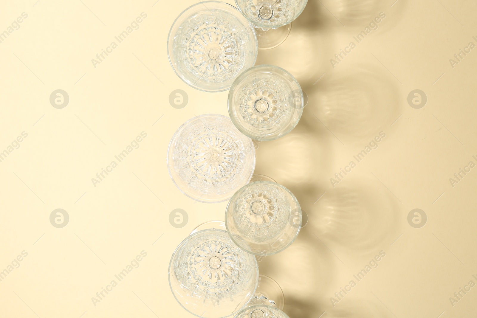 Photo of Empty wine glasses casting beautiful shadows on beige background, flat lay