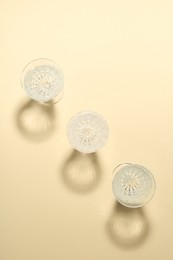 Photo of Empty wine glasses casting beautiful shadows on beige background, flat lay