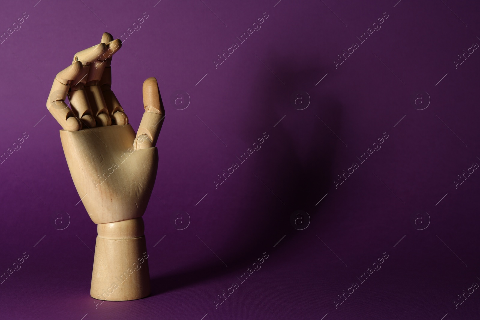 Photo of Wooden mannequin hand on purple background, space for text