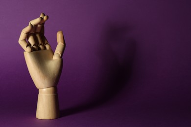 Photo of Wooden mannequin hand on purple background, space for text