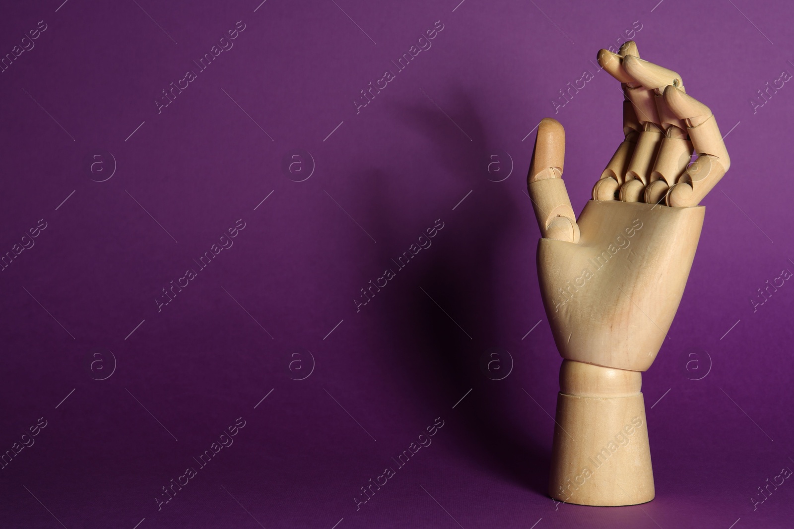 Photo of Wooden mannequin hand on purple background, space for text